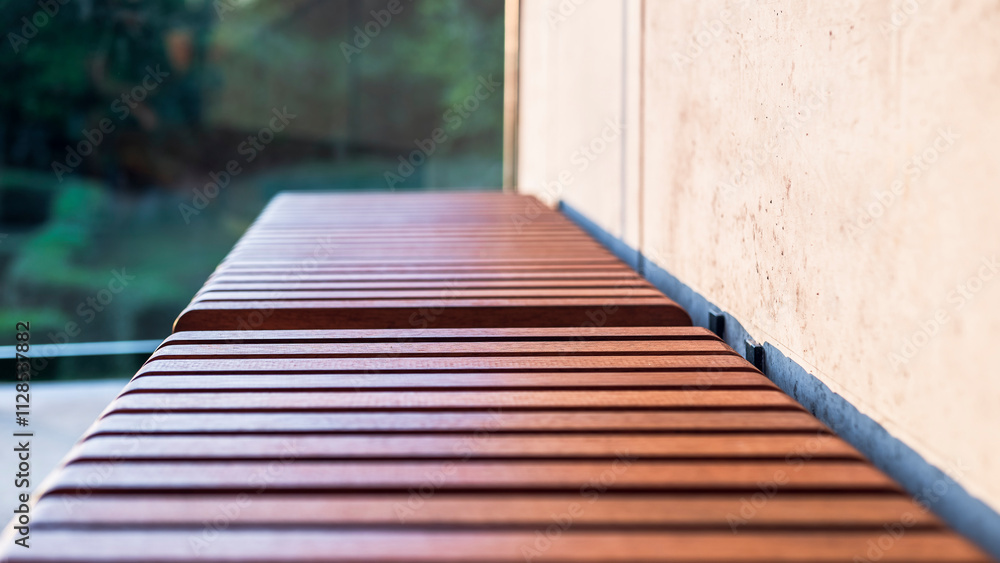 Wooden slats on the bench seat. Exotic Iroko wood. Detail. Close up. Architectural concrete wall and greenery in the background