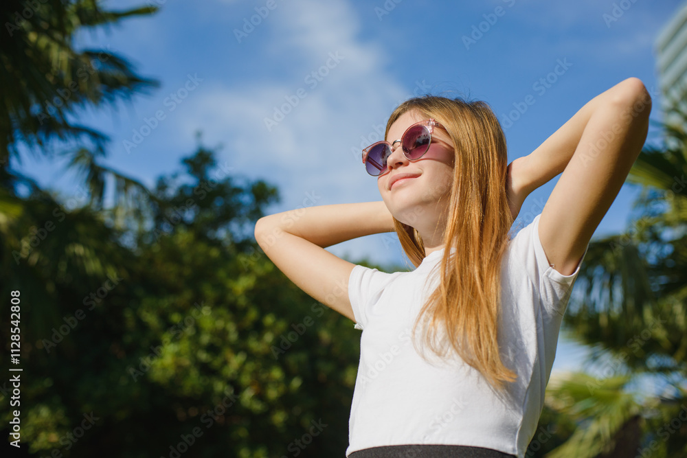 A teenage girl with long hair against the sky in a park wearing a hat and sunglasses A teenage girl with long hair against the sky in a park wearing a hat and sunglasses