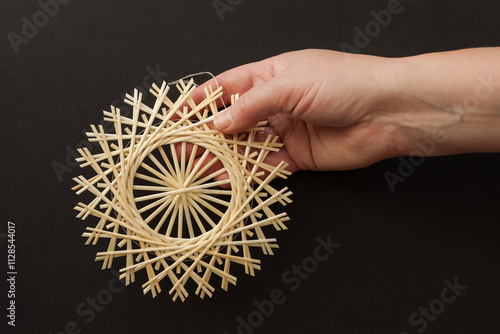 Snowflakes are made of straw in a woman's hand. Snowflakes are made of straw on a black background. Christmas decor. Top view. Straw weaving. 