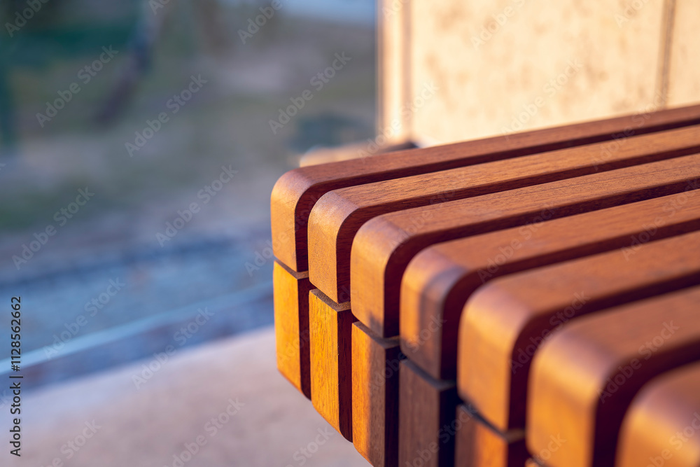 Wooden slats on the bench seat. Exotic Iroko wood. Detail. Close up. Architectural concrete wall. .Warm sunlight illuminates exotic wood