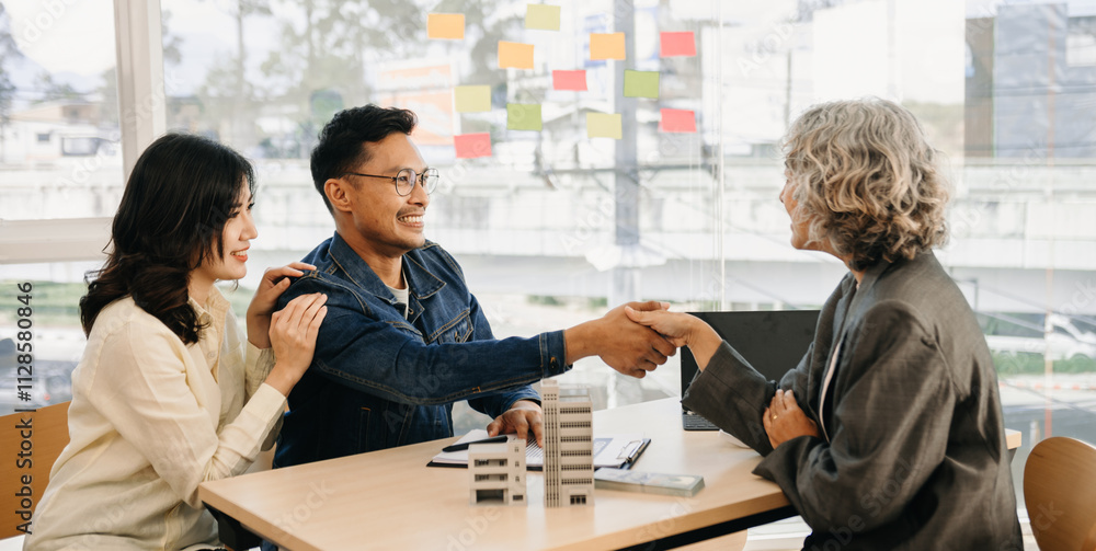 Fototapeta premium Happy couple in love buying house, renting apartment, getting mortgage. Married woman and man meeting with real estate agent, broker, signing agreement for sale