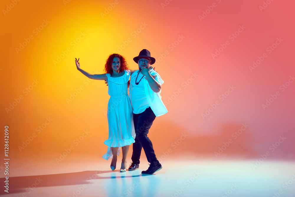 Fototapeta premium Love for dance. Salsa dancers during spirited practice, refining technique and synchronization in neon light against gradient orange background. Concept of dance, performance, art, entertainment.