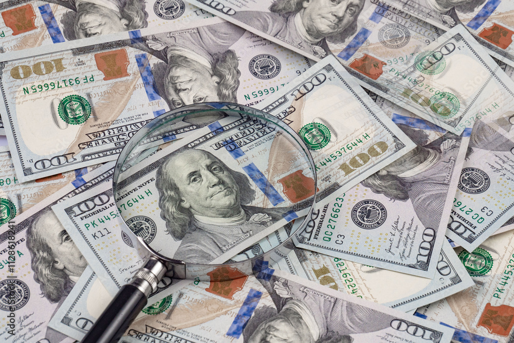 Close up of dollar banknotes and magnifying glass on chart background Close up of dollar banknotes and magnifying glass on chart background