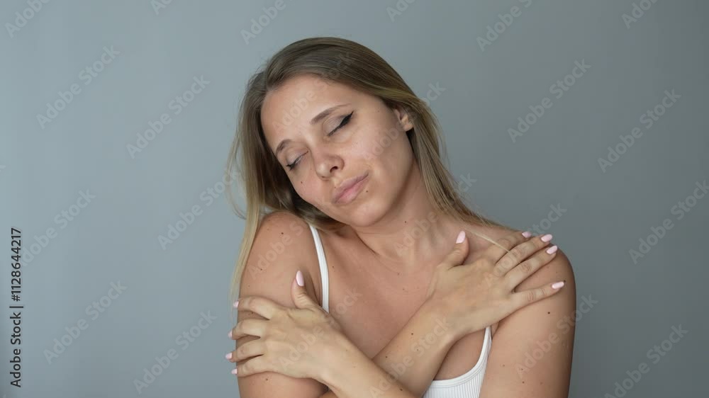 Young attractive caucasian blonde woman hugging herself enjoying the softness of her smooth skin on a dark grey background. Love of self, skin care Young attractive caucasian blonde woman hugging herself enjoying the softness of her smooth skin on a dark grey background. Love of self, skin care