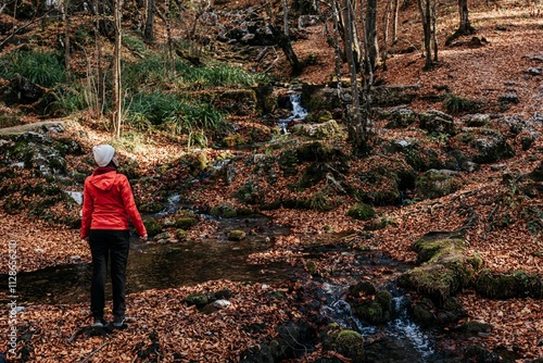 Woman in red jacket by autumn forest stream.