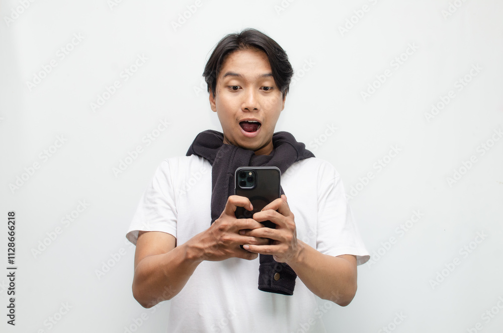 Excited Young Asian Man in Casual Outfit Holding Smartphone with a Joyful Surprise Expression Excited Young Asian Man in Casual Outfit Holding Smartphone with a Joyful Surprise Expression