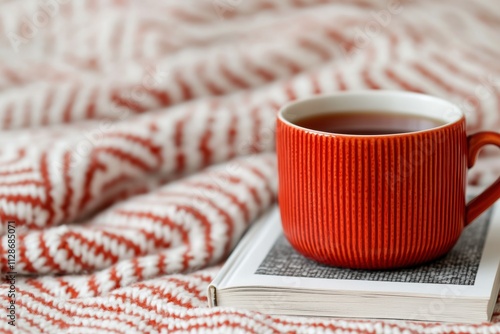 Cozy nook: red mug with herbal tea and book on knitted blanket photo