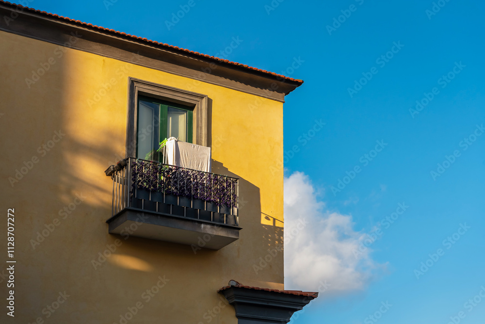 Fragment of a yellow Italian house with a balcony against a blue sky