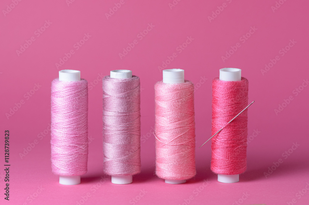Row of many pink thread spools with needle background aligned with copy space for text close-up flat lay top view Row of many pink thread spools with needle background aligned with copy space for text close-up flat lay top view