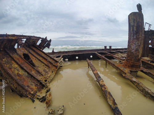 The Rusty Shipwreck lies peacefully on the Sandy Shoreline below a Gloomy Sky with clouds K'gari Fraser Island Australia photo