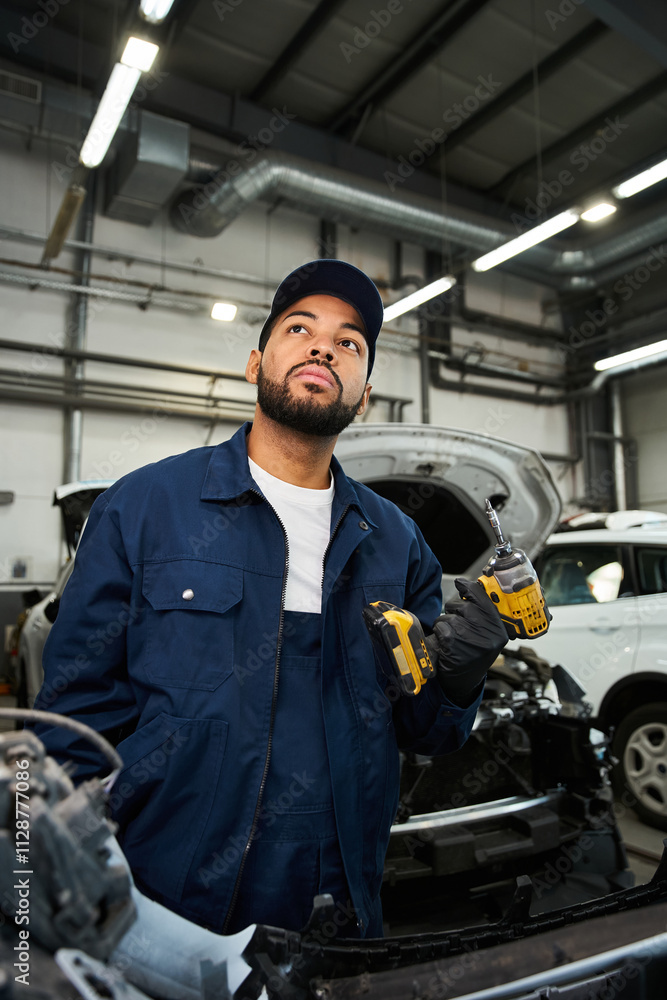 A young mechanic with a thoughtful expression holds tools while working in a bustling garage. A young mechanic with a thoughtful expression holds tools while working in a bustling garage.