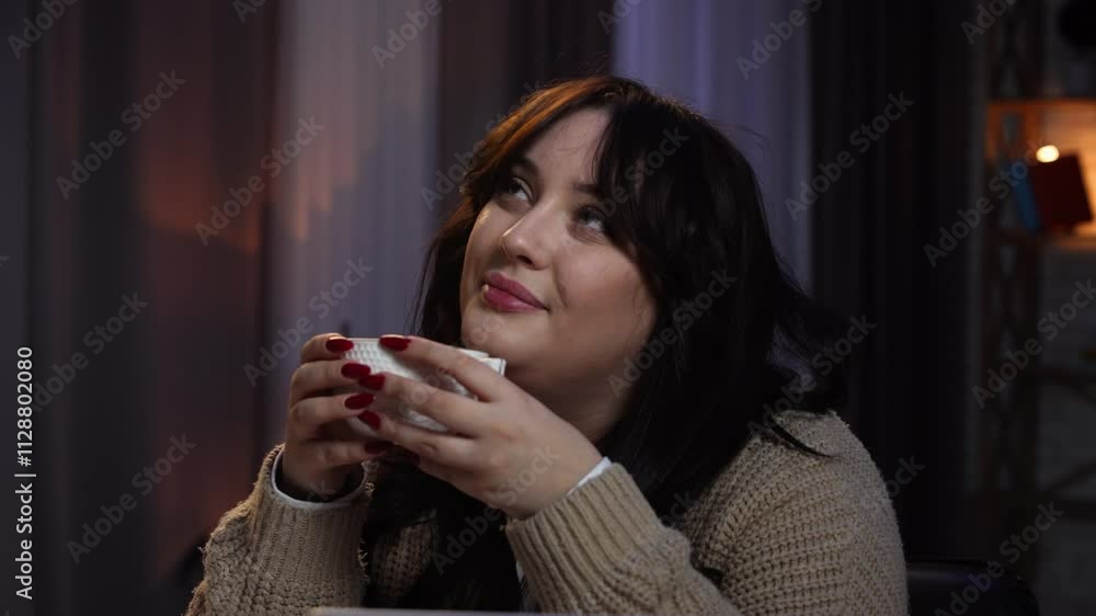 Young business woman freelancer sitting at desk working on remote in home office late using laptop, drinks coffee, dreaming about vacation, positive expression. Close shot. Young business woman freelancer sitting at desk working on remote in home office late using laptop, drinks coffee, dreaming about vacation, positive expression. Close shot.