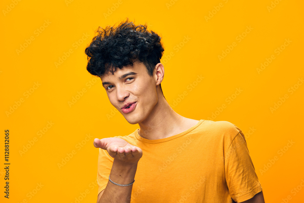Young man blowing a kiss with an inviting smile, set against a bright yellow background that conveys warmth and positivity His casual orange shirt enhances the cheerful vibe Young man blowing a kiss with an inviting smile, set against a bright yellow background that conveys warmth and positivity His casual orange shirt enhances the cheerful vibe
