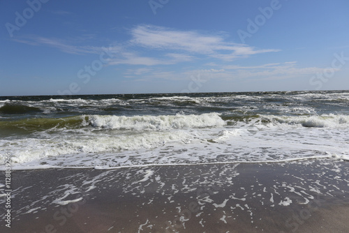 Gentle Waves on a Sunny Beach: A scenic view of ocean waves gently reaching the sandy shore under a clear blue sky, capturing the tranquility and beauty of coastal nature.