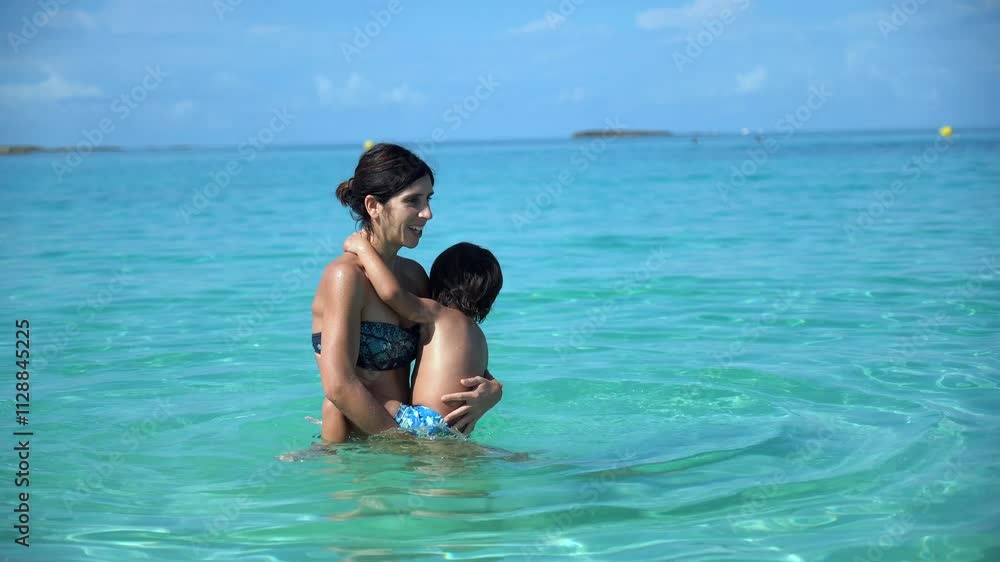 A woman and a child are in the ocean, with the woman holding the child. Scene is joyful and carefree, as the two are enjoying their time together in the water A woman and a child are in the ocean, with the woman holding the child. Scene is joyful and carefree, as the two are enjoying their time together in the water