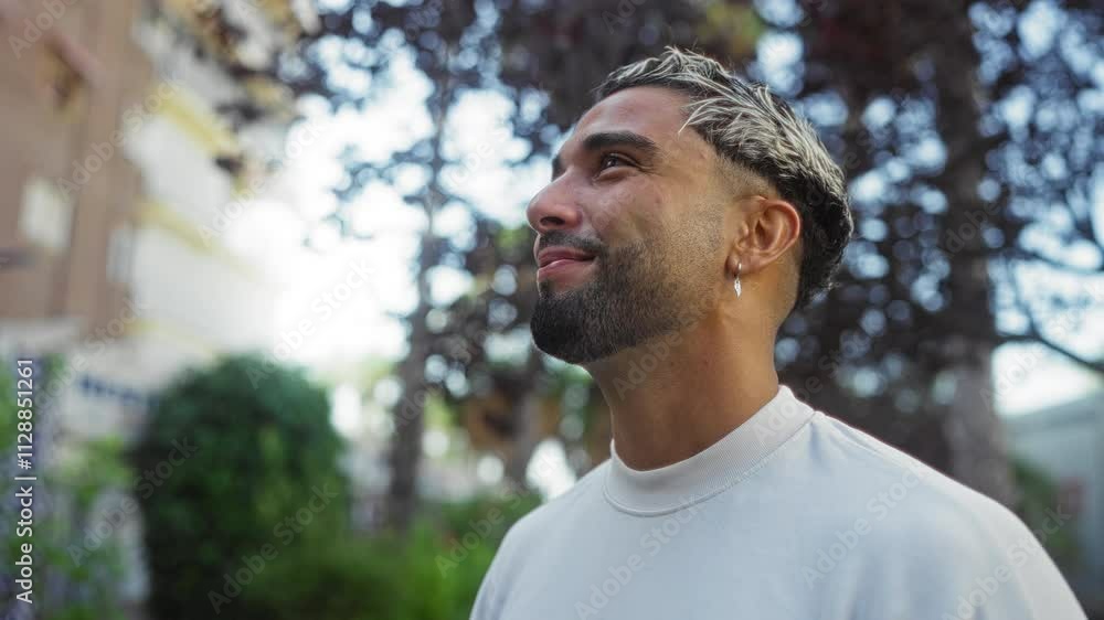 Young arab man with a beard and earrings standing outdoors in an urban park setting, looking serene and contemplative Young arab man with a beard and earrings standing outdoors in an urban park setting, looking serene and contemplative