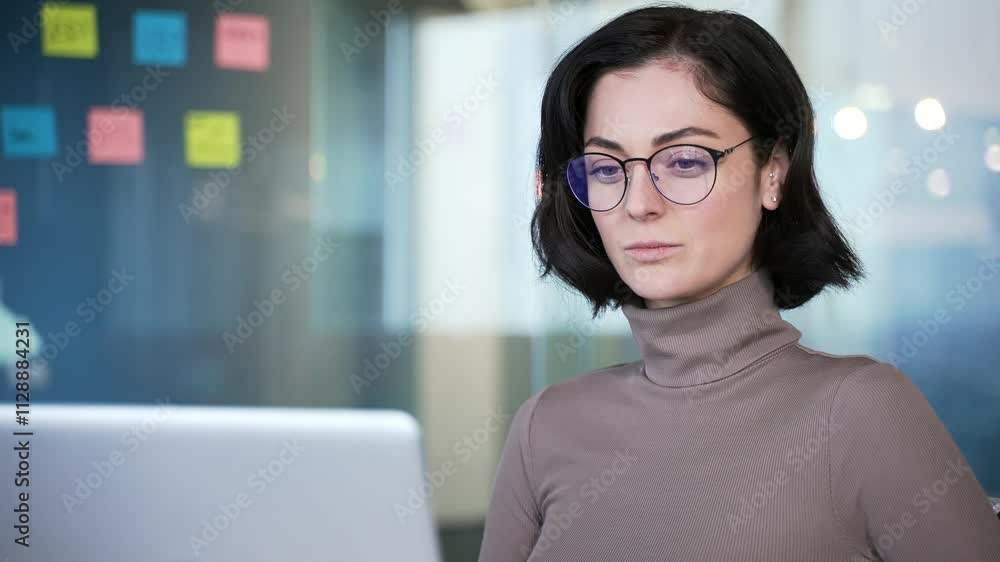 Woman wearing glasses focused on working on her laptop in a modern office. Thoughtful businesswoman professional handling her tasks. while sitting at computer at workplace in business office. Close up Woman wearing glasses focused on working on her laptop in a modern office. Thoughtful businesswoman professional handling her tasks. while sitting at computer at workplace in business office. Close up