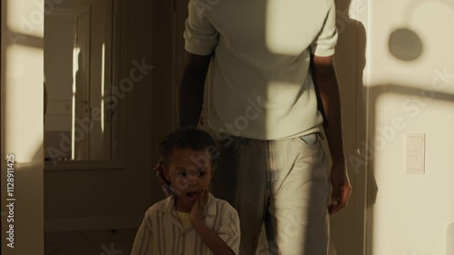 Slowmo tilt up shot of caring young Black father and his son with toy in hand wearing casual clothes entering sunny cozy room at home with modern interior