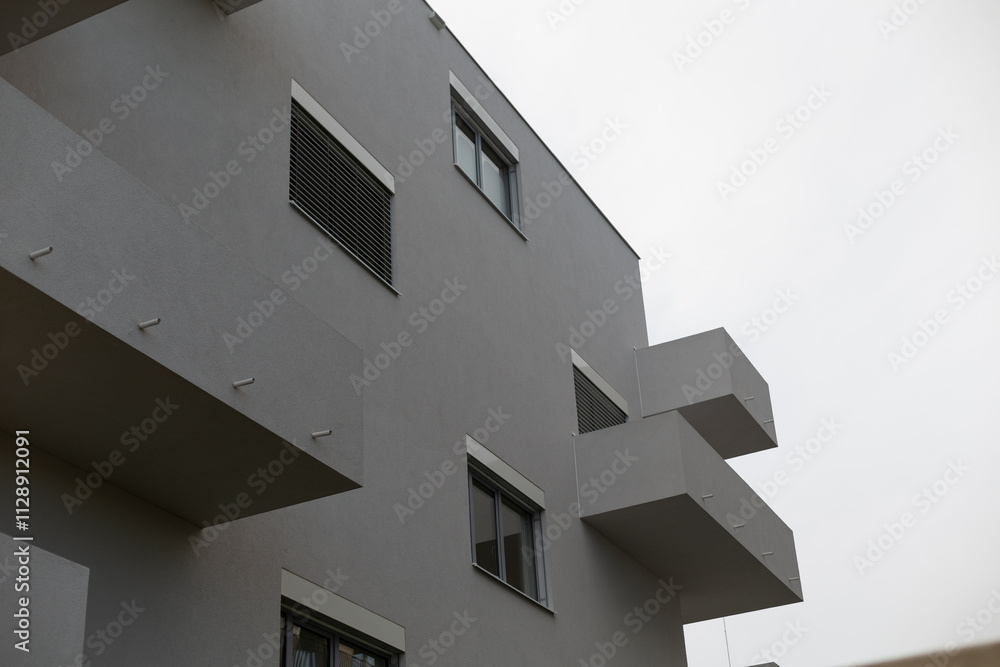 A tall, modern building featuring numerous windows and balconies stands prominently against a backdrop of a cloudy sky filled with gray clouds A tall, modern building featuring numerous windows and balconies stands prominently against a backdrop of a cloudy sky filled with gray clouds
