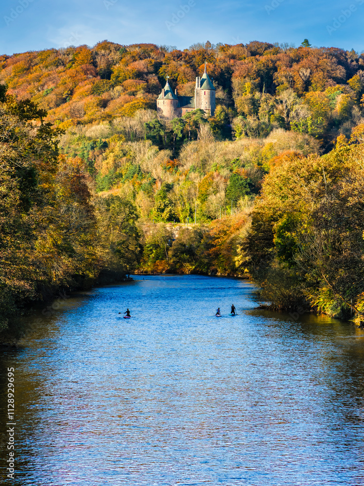 Distant paddleboarders on a river with fairly tale castle and autumn foliage behind (River Taff, Wales) Distant paddleboarders on a river with fairly tale castle and autumn foliage behind (River Taff, Wales)