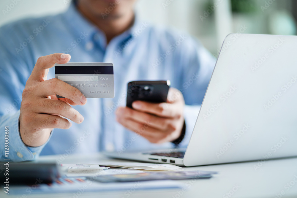 A man is holding a credit card and a cell phone, possibly using them to make a purchase A man is holding a credit card and a cell phone, possibly using them to make a purchase