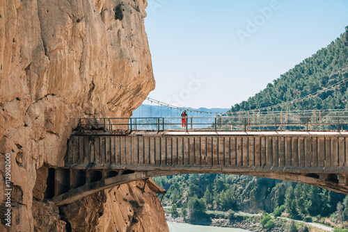 Lonely hiker woman standing on Hanging Bridge over the mountain river and enjoying Spanish Malaga province valey landscape during Caminito del Rey hiking tour in narrow Canyon. South Spain.