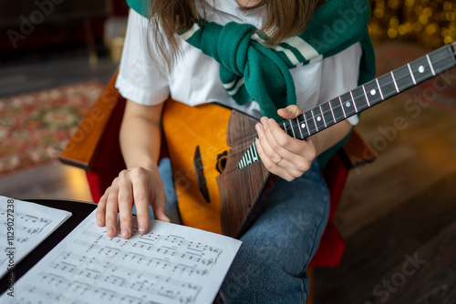 Girl hand flips through sheet music for balalaika. Learning notes and chords for traditional string instrument, practicing at home or in class. Focused on mastering technique, develop musical skill