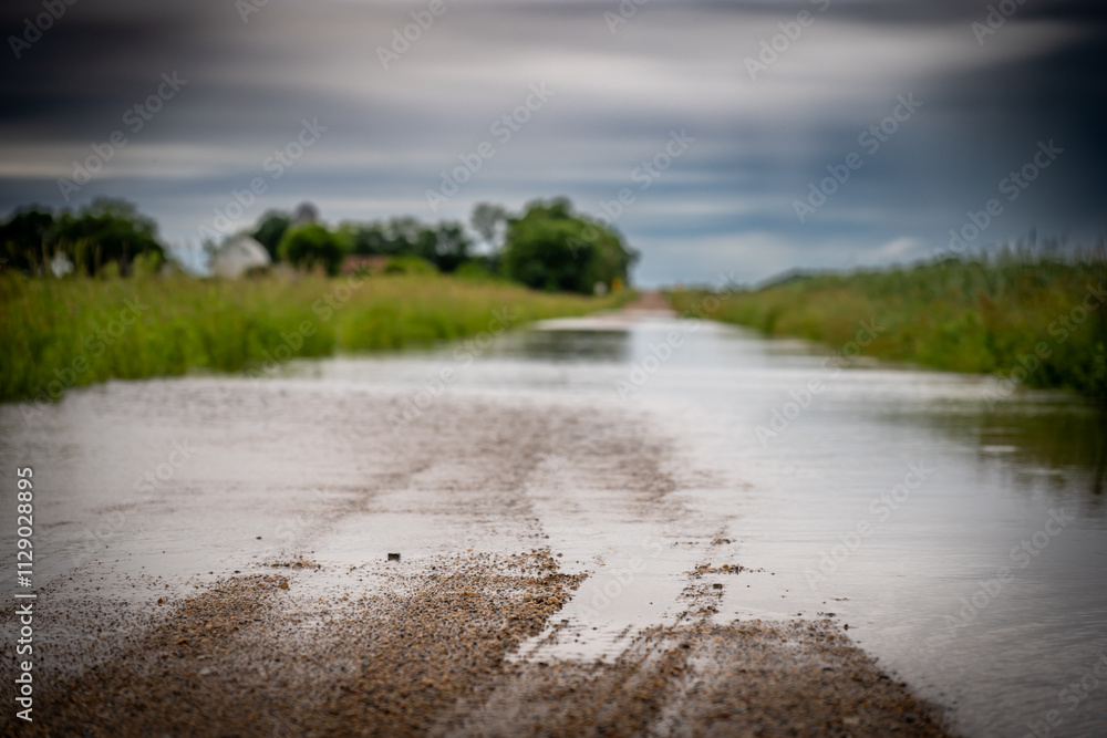 Selective focus on the gravel leading into floodwater covering the road in a rural area Selective focus on the gravel leading into floodwater covering the road in a rural area