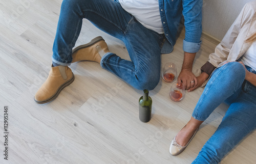 A man and woman are sitting on the floor with a bottle of wine, celebrating your new apartament. New home concept.