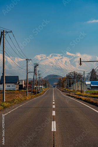 どこまでも続く北海道の一本道と雪化粧の旭岳と紅葉/An endless road in Hokkaido, snow-capped Mount Asahidake and autumn leaves photo