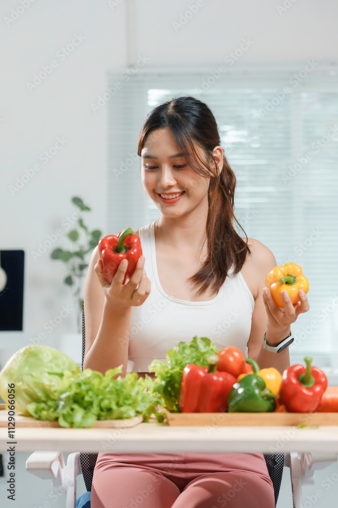 Smiling woman choosing between red and yellow bell pepper while preparing a healthy vegetarian meal or salad in a modern kitchen
