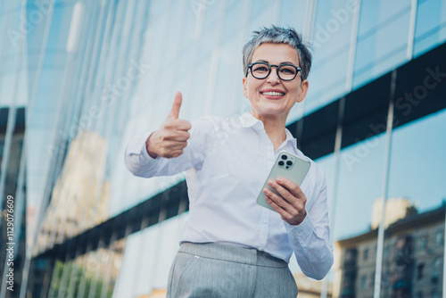 Confident middle-aged businesswoman with grey hair giving thumbs up on urban street in elegant blouse by cityscape Free Download Confident middle-aged businesswoman with grey hair giving thumbs up on urban street in elegant blouse by cityscape - GFXLoad