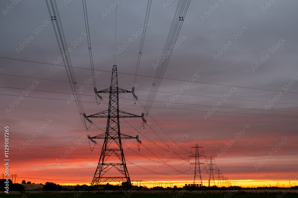 Fototapeta premium Line of electricity pylons at sunrise