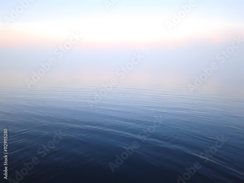 Gentle ripples on a calm lake at dawn, with fog and subtle pink and blue tones in the air