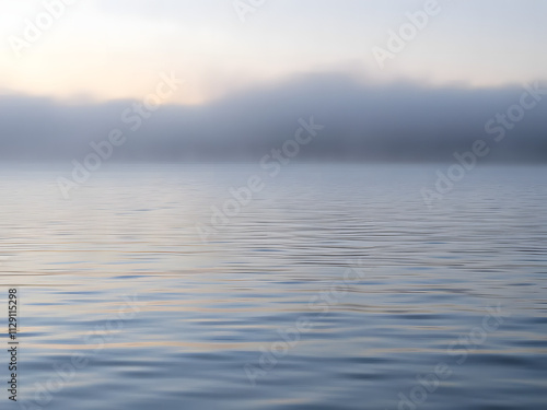 Gentle ripples on a calm lake at dawn, with fog and subtle pink and blue tones in the air