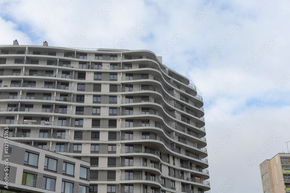 A very large building that features numerous windows stands prominently against a backdrop of an overcast and cloudy sky A very large building that features numerous windows stands prominently against a backdrop of an overcast and cloudy sky