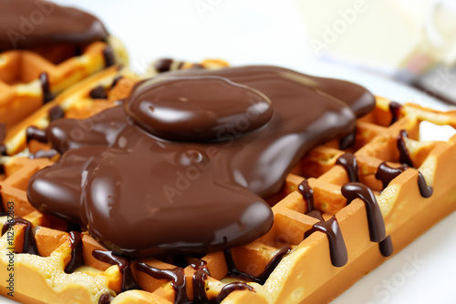 Waffle covered in syrup and drizzled with chocolate. Waffle with white chocolate on a white background. Close up of a waffle with brown sugar and chocolate. Close up of a waffle lifestyle with. photo