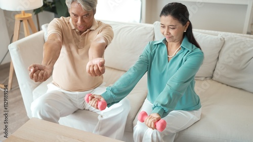 Happy elderly couple exercising together with dumbbells at home, focusing on muscle strength, joint health, and physical wellness for improved mobility and healthy aging. Retirement concept. Myrmidon.