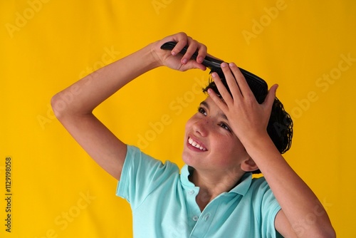 preteen boy on yellow background combing his hair with a black hairbrush photo