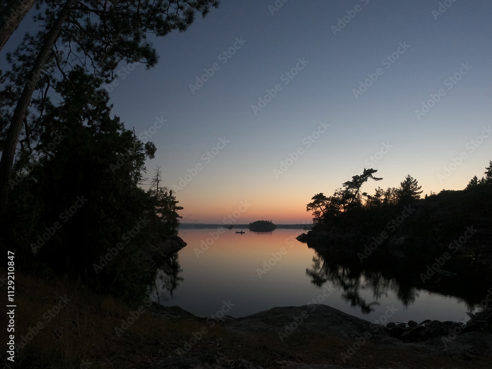 View from a campsite of a solo canoe on a lake in the Boundary Waters Canoe Area (BWCA) at dusk. View from a campsite of a solo canoe on a lake in the Boundary Waters Canoe Area (BWCA) at dusk.
