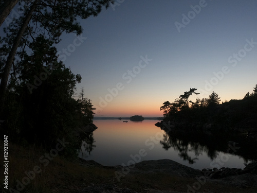 View from a campsite of a solo canoe on a lake in the Boundary Waters Canoe Area (BWCA) at dusk.