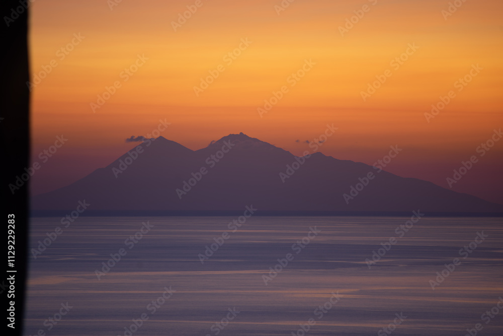 A serene view of a mountain silhouette against a vibrant sunset sky over a calm sea. A serene view of a mountain silhouette against a vibrant sunset sky over a calm sea.