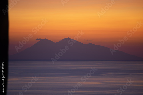 Cuadro en lienzo A serene view of a mountain silhouette against a vibrant sunset sky over a calm sea