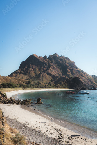 Tourists enjoy a sunny day at the picturesque beach near a rugged mountain landscape.