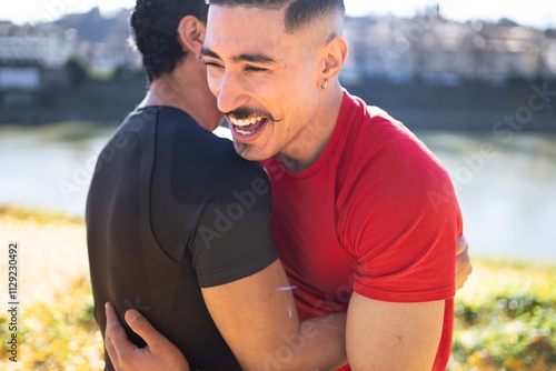 Two men embrace and laugh warmly near a serene riverside trail, surrounded by vibrant foliage and illuminated by golden sunlight on a clear autumn day photo