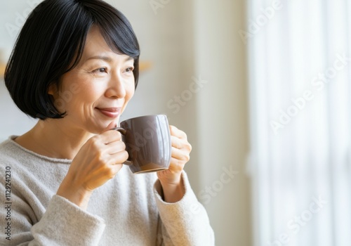 Happy senior woman enjoying a cup of tea or coffee at home, looking out the window with a peaceful expression