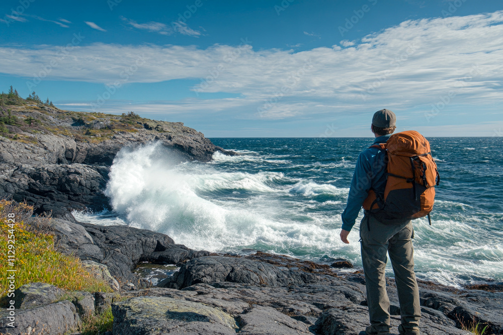 Fototapeta premium Male hiker with backpack exploring rocky ocean coastline on a windy day