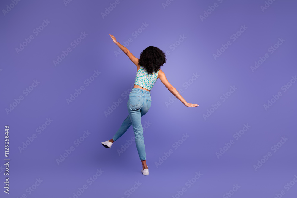 Young woman with afro hair playfully posing against a vibrant purple backdrop, showcasing a stylish summer look in trendy jeans and top Young woman with afro hair playfully posing against a vibrant purple backdrop, showcasing a stylish summer look in trendy jeans and top