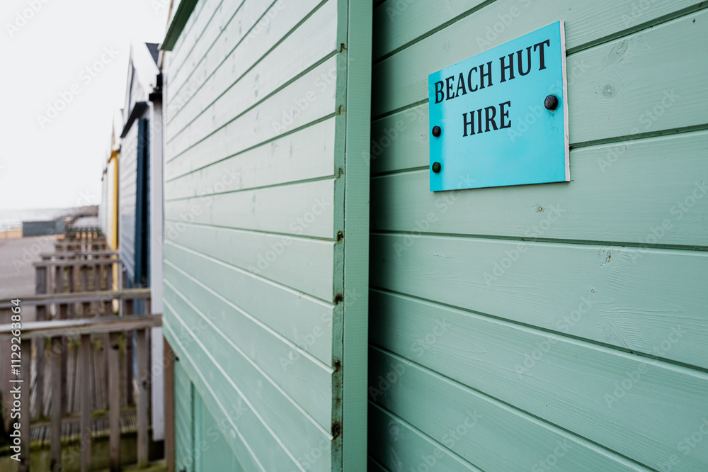 Shallow focus of a line of wet English beachfront huts seen on a winter days day. A For Hire sign is seen on the first beach hut in view. Shallow focus of a line of wet English beachfront huts seen on a winter days day. A For Hire sign is seen on the first beach hut in view.