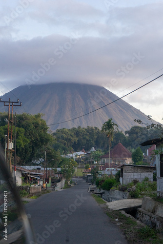 A serene village road with a towering volcano in the background enveloped by clouds. photo